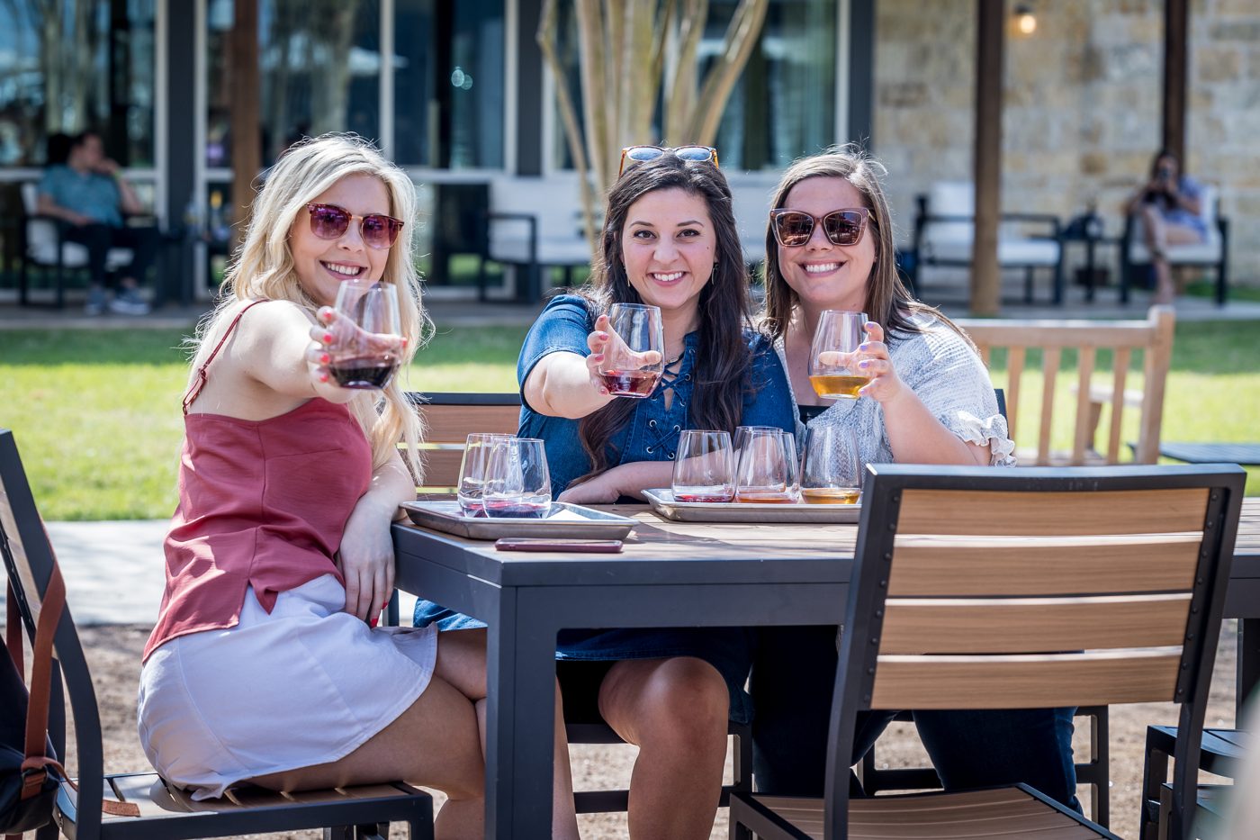 Three friends raising their glasses toward the camera on a winery patio